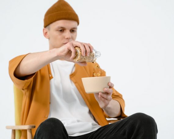 Man in casual wear pouring cereal into a bowl, captured during a studio shoot.